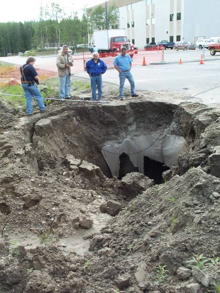 Workers gather around a thermokarst  a hole that opened up due to thawing permafrost beneath  behind a University of Alaska Fairbanks building. (Courtesy Photo / Vladimir Romanovsky)