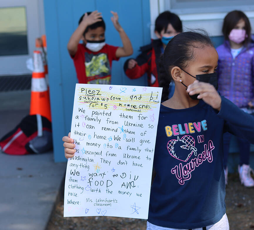 Jasmine Oree, 6, holds up a sign advertising a card stand Friday afternoon outside Sítʼ Eetí Shaanáx̱ - Glacier Valley School. Students in Carly Lehnharts kindergarten class sold cards to community members decorated with pictures of sunflowers, Ukraines national flower, to raise money for a Ukrainian family in Washington state. (Ben Hohenstatt / Juneau Empire)