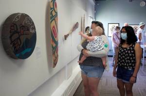 Kristall Bullock, 16, right, a Ketchikan resident whose Native-themed vest is part of the Sealaska Heritage Juried Youth Art Exhibit, examines works by her peers during the debt of the exhibit Friday at the Juneau Arts and Humanities Council. She said she saw works at the exhibit during Celebration in 2018, when she was with one of the dance groups, and I was thinking I want to have a piece. Viewing other works at the exhibit with Bullock are her sister, Anna Lindgren, and 8-month-old niece, Evelyn. (Mark Sabbatini / Juneau Empire)