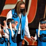 Triplets Liam, Lawrence and Logan with their mother Lory David wave to the crowd at Centennial Hall on Friday, June 10, 2022, during Celebration 2022s Toddler Regalia Review, featuring kids aged 2-5 wearing traditional clothing. (Peter Segall / Juneau Empire)