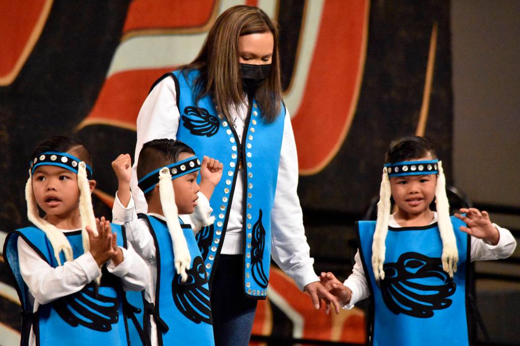 Triplets Liam, Lawrence and Logan with their mother Lory David wave to the crowd at Centennial Hall on Friday, June 10, 2022, during Celebration 2022s Toddler Regalia Review, featuring kids aged 2-5 wearing traditional clothing. (Peter Segall / Juneau Empire)