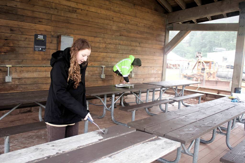 Kali Braning, left, a University of Utah student, and Derek Thompson, a Michigan Tech student, paint picnic tables beneath a shelter at Savikko Field on Monday in preparation for Juneau Gold Rush Days. (Mark Sabbatini / Juneau Empire)