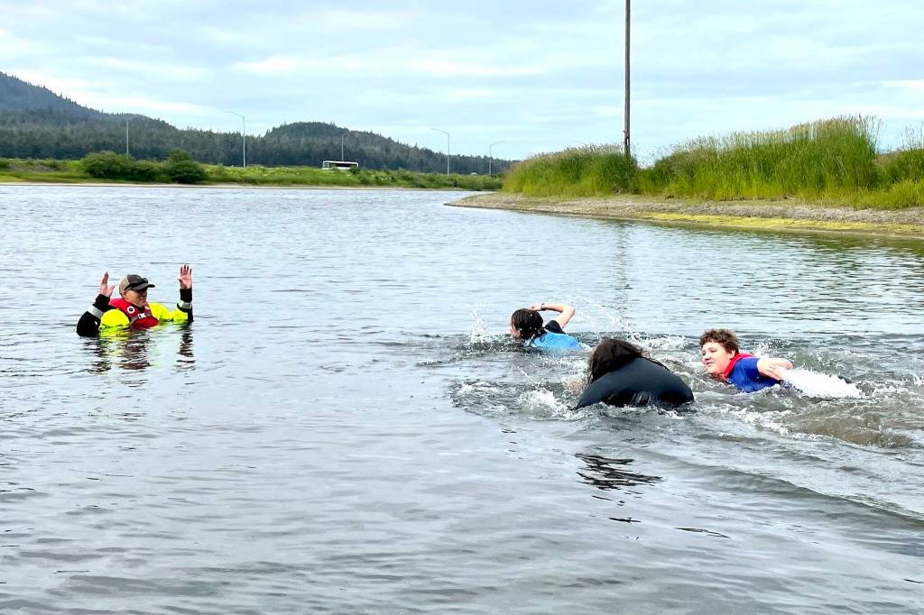Kids wearing a variety of personal flotation devices swim to Coast Guard Lt. J.J. Cestero as part of a boating safety class in Twin Lakes on June 30, 2022. (Michael S. Lockett / Juneau Empire)