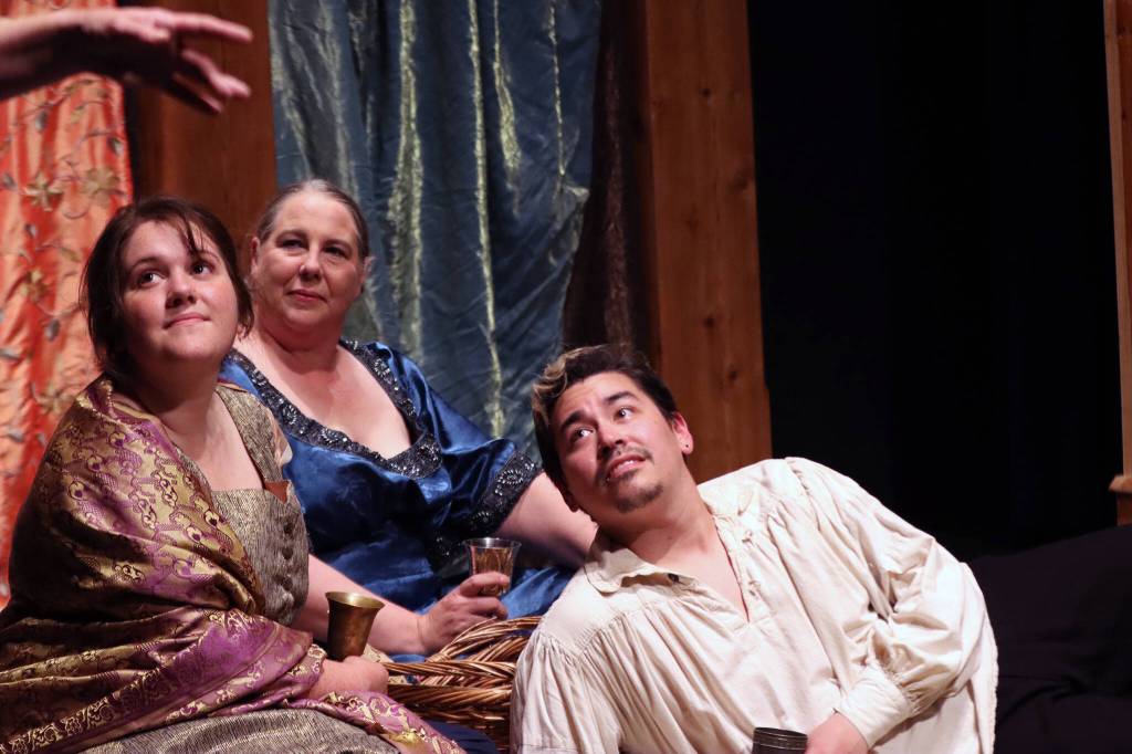 Hero (Lily Ayau), Leonate (Valleri Collins) and Claudio (Ty Yamaoka) listen to a song while enjoying food and libation ahead of Hero and Claudios planned marriage. (Ben Hohenstatt / Juneau Empire)