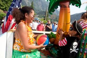 Rachel Hurst hands her son Benjamin, 4, a beach ball to throw to the crowd from the Hawaiian-themed Juneau Urgent Care float during the July 4 parade in downtown Juneau. (Mark Sabbatini / Juneau Empire)