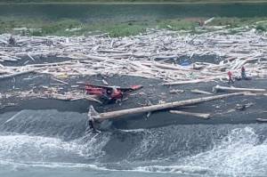 A P-18 Super Cub aircraft and two people on shore at Montague Island, Alaska, after the plane crashed July 6, 2022. (U.S. Coast Guard / Lt. Cmdr. Josh Wofford)