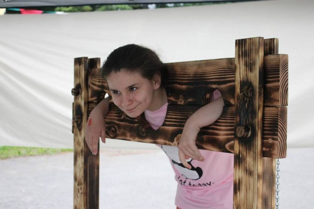 Chloe Dees poses for a picture in a mock pillory device outside at the Masters Faire. (Clarise Larson // Juneau Empire)
