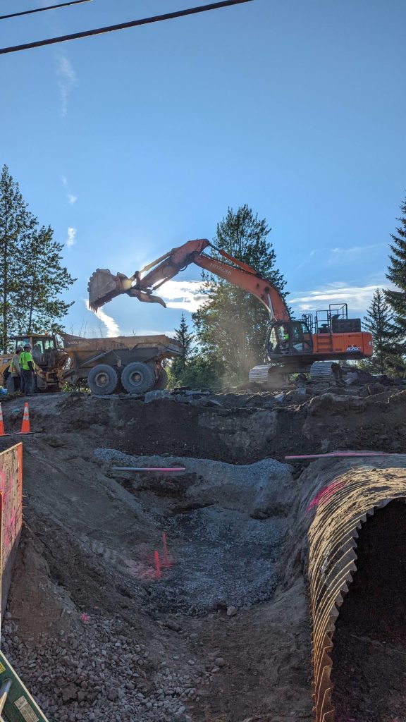 An excavator dumps dirt into a dump truck as crews perform work near Mendenhall Loop Road on Friday, July 15, 2022. (Courtesy photo / Sam Dapcevich)
