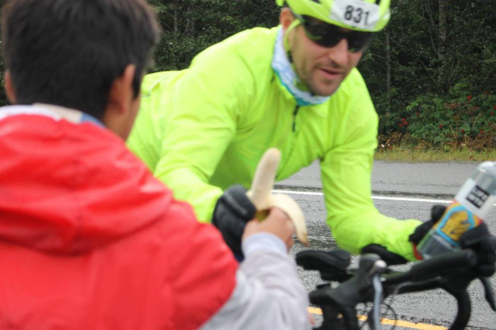 Edgar Vera, a junior student at Juneau-Douglas Yadaa.at Kalé High School track team, hands out free peeled bananas to passing racers. He and other track students are volunteering to raise funds for their coming seasons travel costs. (Clarise Larson/ Juneau Empire)
