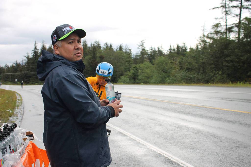 Louis Tagaban, a head coach for Juneau-Douglas Yadaa.at Kalé High School track team helps give a racer food and water at the aid station manned by the team. (Clarise Larson/ Juneau Empire)