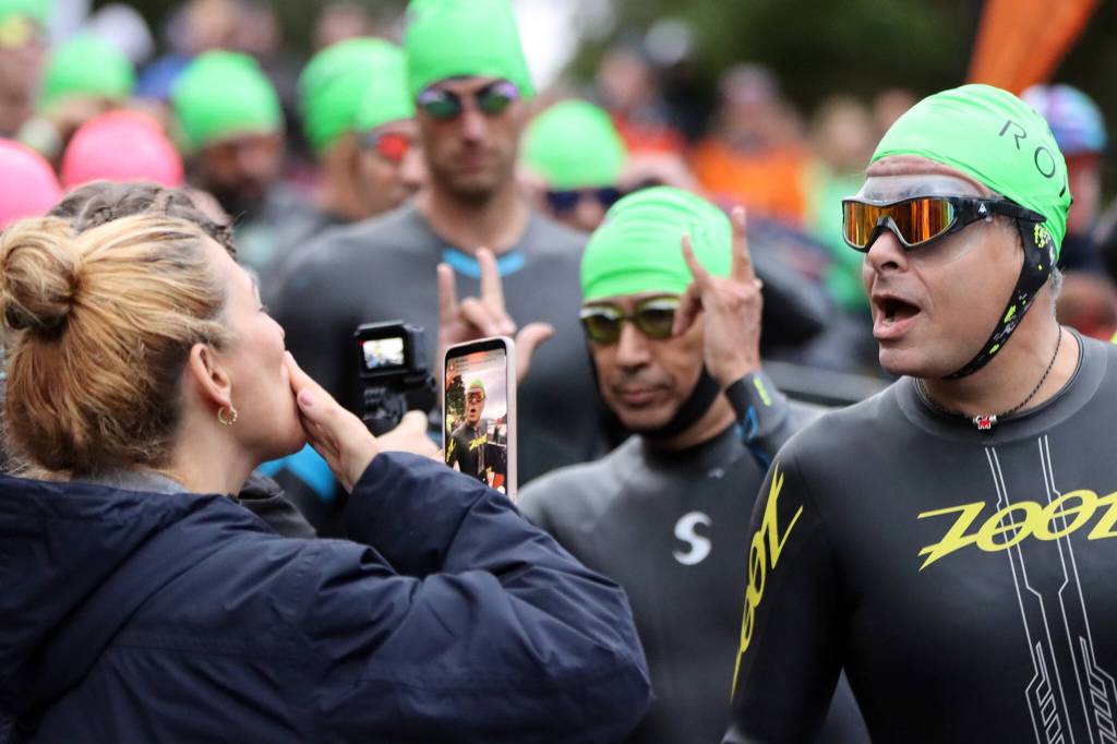 A supporter blows a kiss to an Ironman Alaska athlete who reacts with enthusiasm while a nearby athlete throws up a rocknroll salute. (Ben Hohenstatt / Juneau Empire)