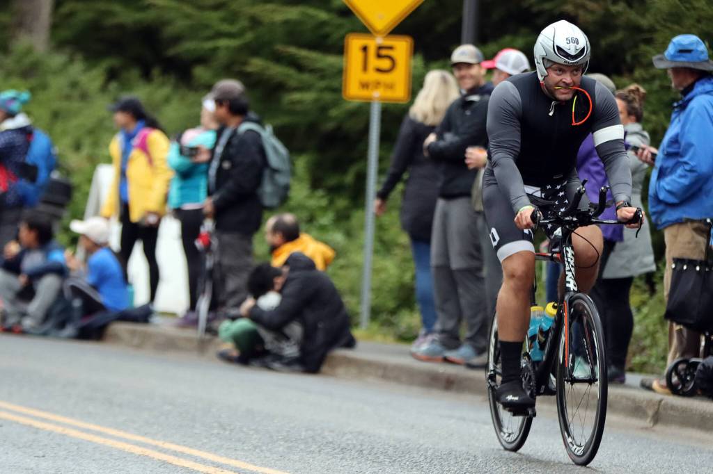 Nicholas Schaefer bikes past onlookers early on in the bicycle leg of Ironman Alaska. Many passing cyclists could be seen getting in a quick bite to eat or gulping refreshments near the start of the 112-mile course. (Ben Hohenstatt / Juneau Empire)