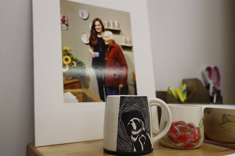 A photo of Mercedes Muñoz and her late grandmother and the galley namesake Rie Muñoz sits in the studio behind a mug featuring one of Muñozs dogs. The photo was taken at Mercedes Muñoz first solo show which took place only three days before her grandmother passed away in 2015. (Clarise Larson / Juneau Empire)