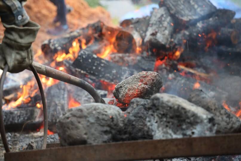 Students pull the lava rocks out of the fire using shovels. The group spent the day rotating the rocks in order to have them as hot as possible to boil the water. (Clarise Larson / Juneau Empire)