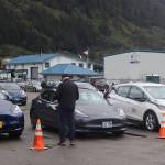 An attendee looks at a parking lot of electric vehicles during the ninth annual Juneau EV & EBIKE Roundup on Saturday. While a rally with the vehicles was scheduled through the streets of Juneau and Douglas as part of the event, it was canceled as many attendees left early due to rainy and windy weather. (Mark Sabbatini / Juneau Empire)