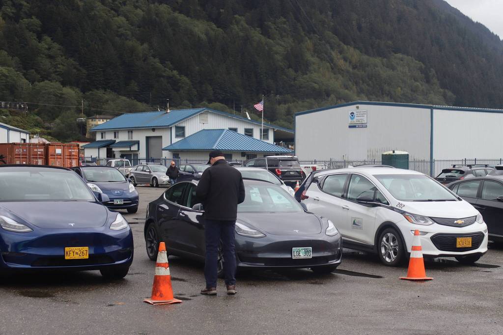 An attendee looks at a parking lot of electric vehicles during the ninth annual Juneau EV & EBIKE Roundup on Saturday. While a rally with the vehicles was scheduled through the streets of Juneau and Douglas as part of the event, it was canceled as many attendees left early due to rainy and windy weather. (Mark Sabbatini / Juneau Empire)