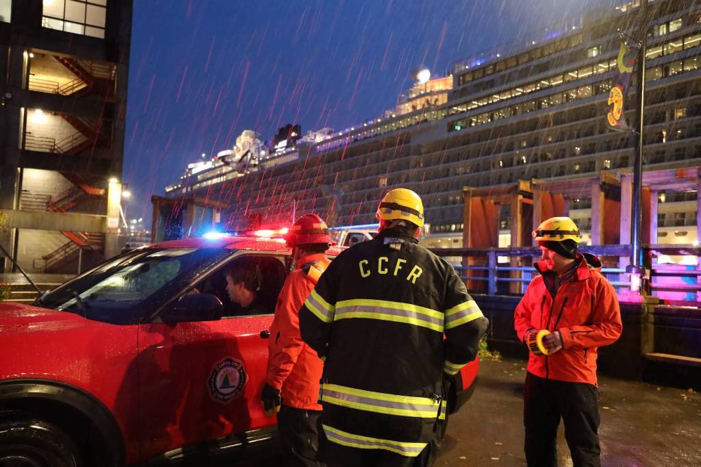 CCFR assistant chief Sam Russell and other officials talk in the rain outside of the Juneau Public Library in downtown. Residents were just starting to arrive at the staging tents around 7 p.m.(Clarise Larson / Juneau Empire)