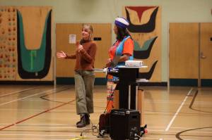 Laura Talpey, executive director of Juneau Montessori School speaks into the mic next to Jamiann Seiltin Hasselquist, vice president of Alaska Native Sisterhood Camp 2 Juneau, in front of a crowd gathered at Sayé ik: Gastineau Community School Wednesday evening. ( Clarise Larson / Juneau Empire)