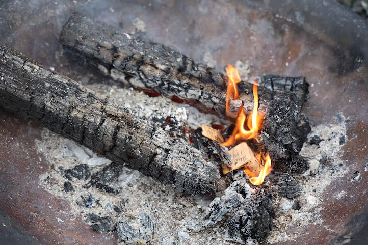 Wood chips burn in a fire pit during the event. People were allowed to write names on chips from the project, which then were burned with the hope that the act brings healing to the person whose name was written on the wood. (Clarise Larson / Juneau Empire)