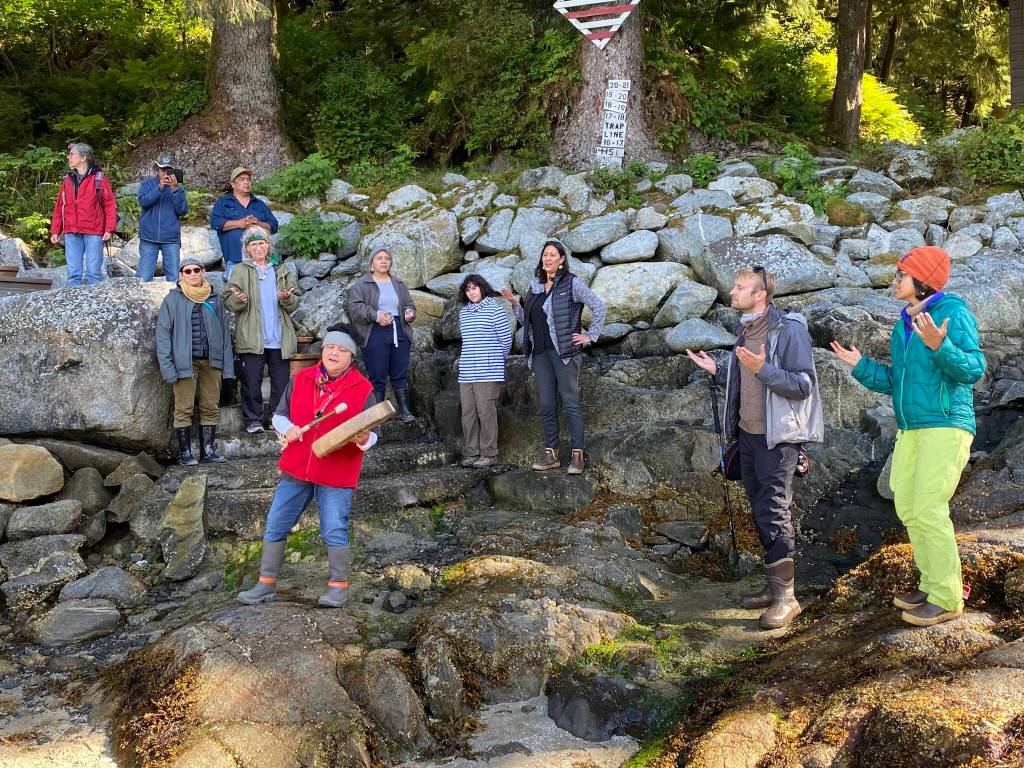 Those gathered on the beach at Anan Creek, joined in song with Virginia Oliver leading on drum, were among the 42 people from the conference who joined the tour of the cultural sites there, led by archeologists of the U.S. Forest Service. (Peter Metcalfe / Sharing Our Knowledge Conference)