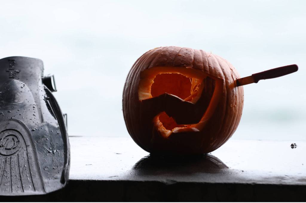 A jack-o-lantern depicting goggles and a snorkel rests on a ledge next to damp flippers on Sunday at Auke Recreation Area. (Ben Hohenstatt / Juneau EmpireP)
