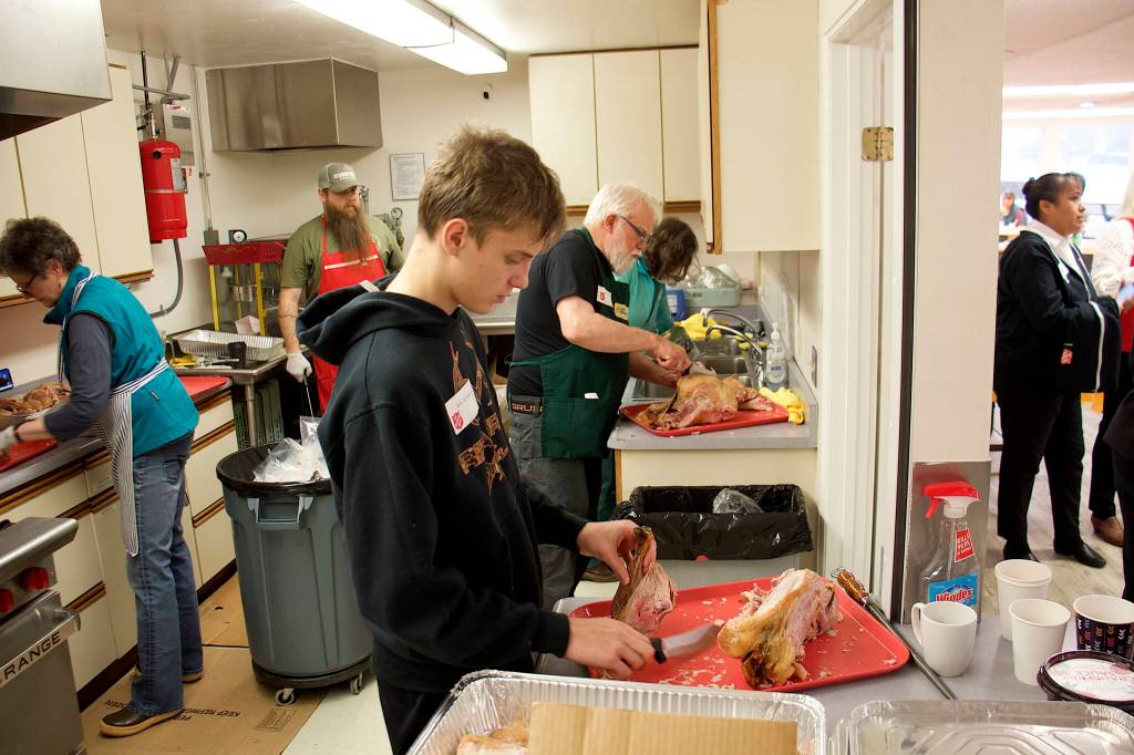 Caleb Friend, 16, and his grandfather, Jerry Harmon, carve turkeys in the kitchen of the Juneau Yacht Club before the serving of the annual communal Thanksgiving dinner at the Juneau Yacht Club. Friend, one of nine members of Harmons family volunteering during the day, said he has been helping since he started wrapping silverware at the age of six. Fifty turkeys were smoked for the gathering by Dick Hand, owner of Alaska Seafood Company. (Mark Sabbatini / Juneau Empire)