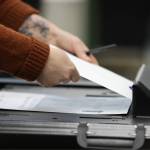An election official helps a voter feed their completed and sealed ballot into the ballot box on Election Day 2022. (Ben Hohenstatt / Juneau Empire File)