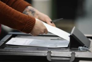 An election official helps a voter feed their completed and sealed ballot into the ballot box on Election Day 2022. (Ben Hohenstatt / Juneau Empire File)