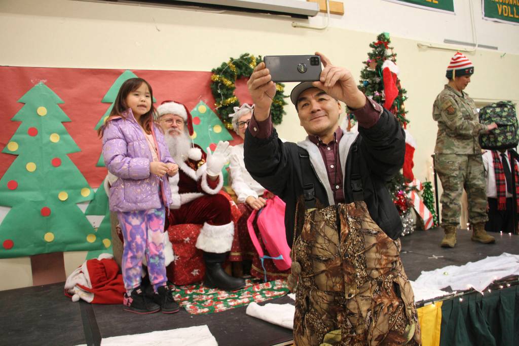 A parent takes a selfie with a child and Santa and Mrs. Claus in Nuiqsut, Alaska, on Nov. 29, 2022. Operation Santa Claus, the Alaska National Guards outreach program, attempts to bring Santa and Mrs. Claus and gifts to children in two or three Alaska Native villages each year, including Nuiqsut in 2022. (AP Photo / Mark Thiessen)
