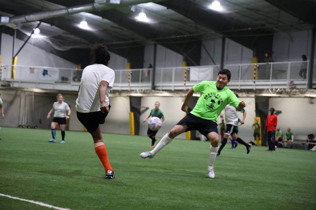 Rachelle Garrett kicks the ball over the leg of opposing player, Ariel Barrios, during a soccer match Monday evening at the Diamond Park Field House a part of the Holiday Cup soccer tournament. (Clarise Larson / Juneau Empire)