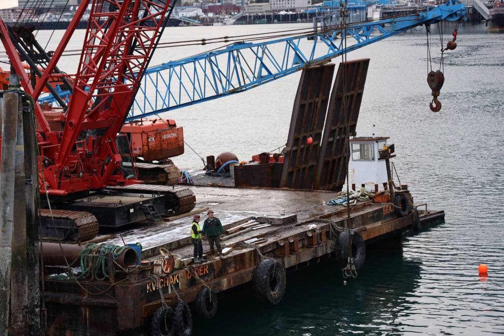 Workers stand on at the edge of a barge that was brought to Juneau to remove the privately owned 107-foot tugboat, theTagish, that sank south of the downtown cruise ship docks in late December. (Clarise Larson / Juneau Empire)