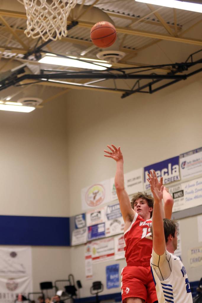 Wrangell senior Ethan Blatchley (12) launches a high-arcing shot over the arms of Petersburg senior Kyle Biggers (23) for two. (Ben Hohenstatt / Juneau Empire)