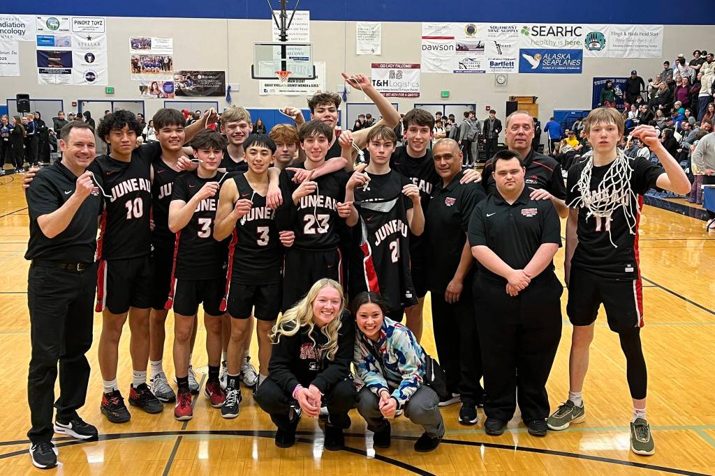 The JDHS Crimson Bears basketball team poses for a victory photo after the net cutting ceremony on Saturday. The Bears beat Ketchikan High School in a second tournament game, securing the teams spot at state. (Jonson Kuhn / Juneau Empire)