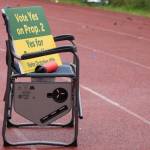 Signs encouraging voters to support Proposition 2, which OKd $6.6 million in bond debt for recreation improvements, sit in a chair on the track at Adair-Kennedy Memorial Park ahead of a football game last fall. Monday evening, the City and Borough of Juneau Assembly approved issuing the bond debt, but concern was expressed about whether field work would involve artificial turf. (Ben Hohenstatt / Juneau Empire File)