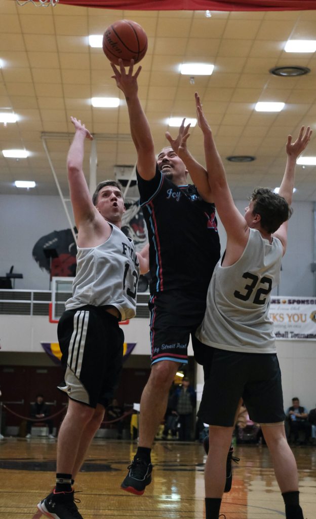 Hoonahs Travis Dybdahl scores between Filcoms Tom Gisler (13) and Charlie Herrington (32) during C Bracket action in the Gold Medal Basketball Tournament, Monday, March 20, at Juneau-Douglas High School: Yadaa.at Kalé. (Klas Stolpe / For the Juneau Empire)