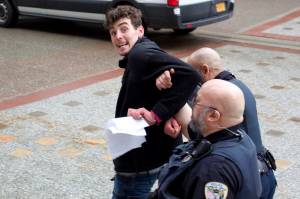 Eric Osuch tries to offer papers related to his arrest in front of the Alaska State Capitol on Monday morning to a reporter as Juneau Police Department officers escort him to a nearby patrol vehicle. Osuch, who was staging a solo protest about fisheries bycatch policies, was banned from the Capitol after causing a public disruption and was arrested a short time later for another alleged disturbance inside the State Office Building. (Mark Sabbatini / Juneau Empire)