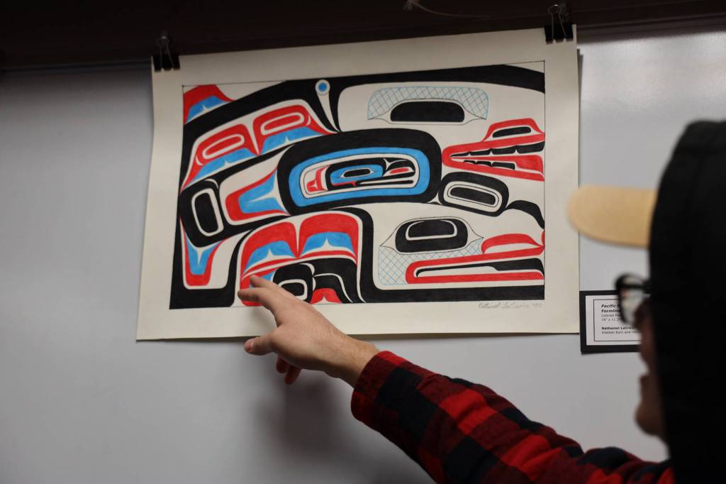 Alaska artist Nathaniel LaCroix explains the design of the piece Pacific Northwest Coast Form-line Swimming Spirit to gallery viewers Friday evening. The piece was one of the many featured in a recent art gallery hosted Friday evening at the University of Alaska Southeast that showcased students work from the UAS Northwest Coast Art program. (Clarise Larson / Juneau Empire)