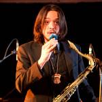 Tenor saxophonist Rico Jones wears a Tlingit Tinaa, given to him and other band members by local students during a visit to Dzantiki Heeni Middle School, as he introduces a song he composed during a concert by the Julia Keefe Indigenous Big Band on Friday night at Elizabeth Peratrovich Hall. (Mark Sabbatini / Juneau Empire)