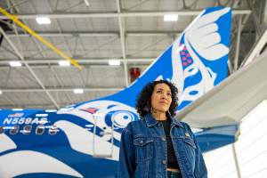 Courtesy Photo / Alaska Airlines
Juneau artist Crystal Kaakeeyáa Worl, who is Tlingit and Athabascan, poses with an Alaska Airlines 737-800 aircraft decorated with Worls latest work, Xáat Kwáani (Salmon People). Alaska Airlines held a unveiling ceremony on Friday, May 12 to welcome the plane into service.