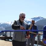 City and Borough of Juneau Docks and Harbors board vice chairman Jim Becker cuts a ribbon Monday afternoon stretched across the Seawalk downtown in celebration of the citys completion of the Docks and Harbors Marine Deckover Project. (Clarise Larson / Juneau Empire)
