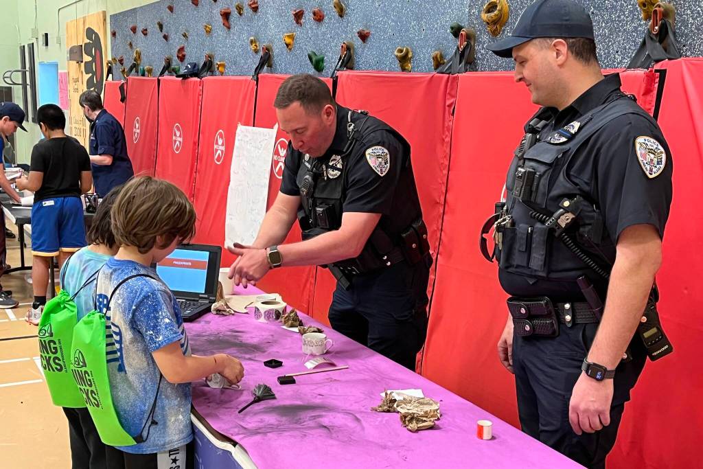 Juneau Police Department Officers John Cryderman and Aron Landry volunteer their time with students for a Fingerprinting station on Thursday for Sayéik: Gastineau Community Schools STEAM event. (Jonson Kuhn / Juneau Empire)