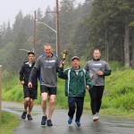Branden Forst (left center) carries the torch with C.J. Umbs (right center) before crossing the finish line during the Alaska Law Enforcement Torch Run at Twin Lakes Park Saturday morning. (Clarise Larson / Juneau Empire)