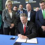 Gov. Mike Dunleavy signs legislation allowing the state to set up a carbon offset program Tuesday in Anchorage. Dunleavy signed the bill with Alaska lawmakers and administration officials standing behind him during the Alaska Sustainable Energy Conference at the Denaina Civic and Convention Center in downtown Anchorage. (AP Photo/Mark Thiessen)