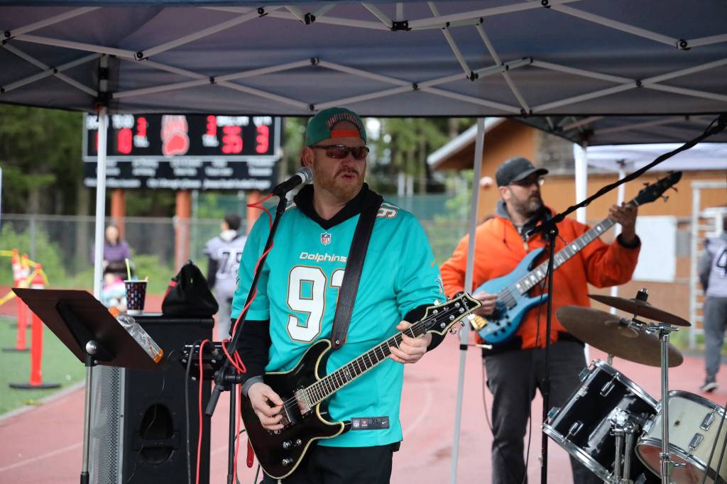 Sean Purvis-Carey rocks out alongside Father Figure bandmates Kyle Bischoff, Brandon Hard and Johnny Perrin during a half-time performance at the Juneau Alumni Football game on Friday at Adair-Kennedy Memorial Park. (Clarise Larson / Juneau Empire)