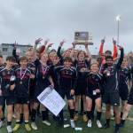 The Juneau-Douglas High School: Yadaa.at Kalé Crimson Bears boys soccer team pose with their championship trophy after defeating Soldotna 4-0 for the ASAA DII Boys Soccer State Championship, Saturday, at West Anchorage High School (Courtesy Photo / JDHS Soccer)