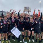 The Juneau-Douglas High School: Yadaa.at Kalé Crimson Bears boys soccer team pose with their championship trophy after defeating Soldotna 4-0 for the ASAA DII Boys Soccer State Championship, Saturday, at West Anchorage High School (Courtesy Photo / JDHS Soccer)