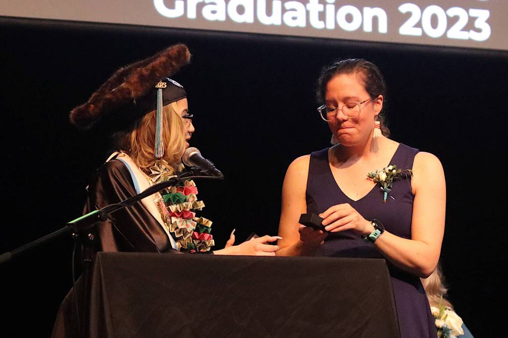 Helen John, the student speaker at Yaakoosgé Daakahídi High Schools graduation on Sunday, presents a tinaa as a farewell gift to Devin Tatro, who is departing as a teacher and adviser at the school. (Mark Sabbatini / Juneau Empire)