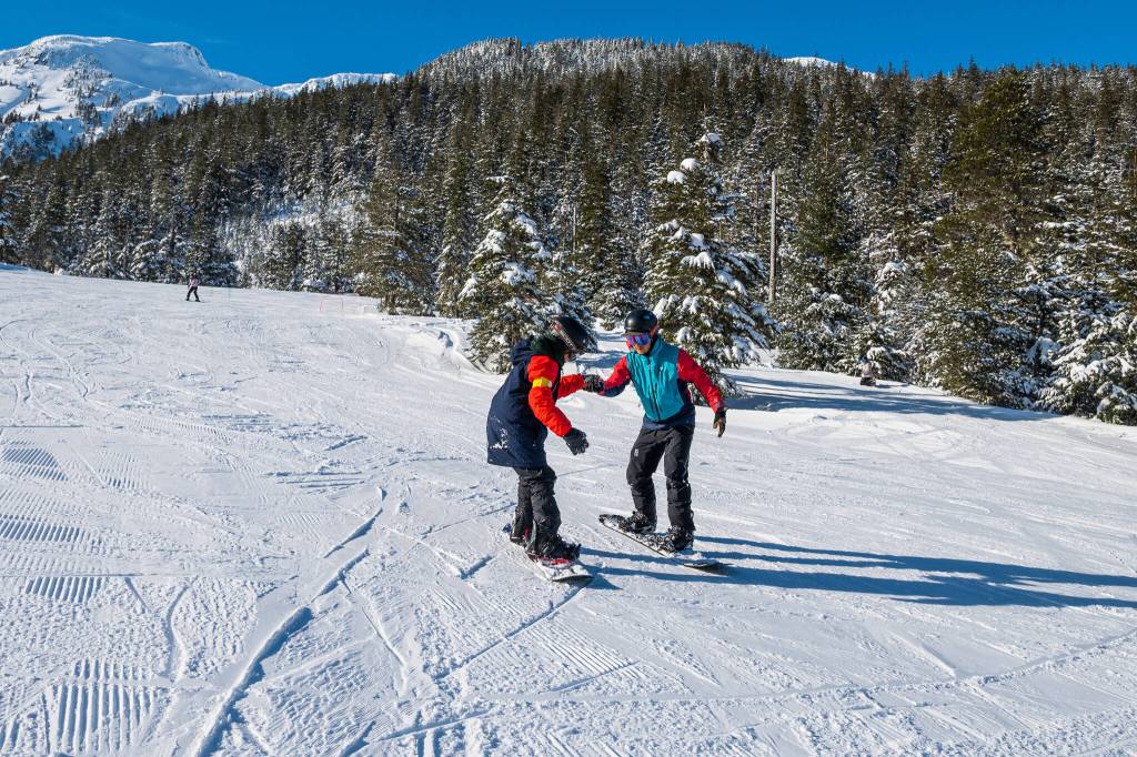 Sitka participant Reece Howard (left), on one of his first runs holds hands for support with chaperone Lee House (right). (Photo by Lione Clare / Sitka Conservation Society)