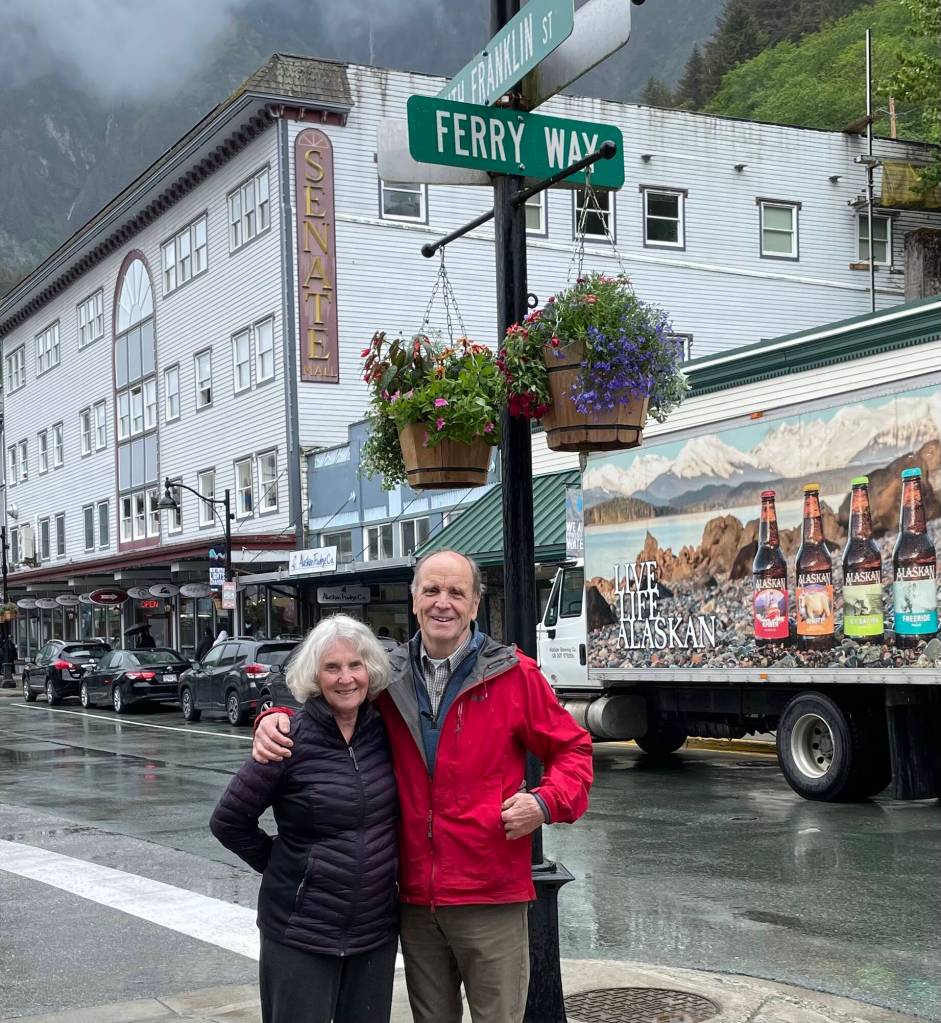 On a damp May 2023 morning, Sharon and Bruce Denton stand before their Senate Building renovation project completed in 1984. Juneaus Downtown Historic District has been rejuvenated in the ensuing years, burying unsightly utility wires, adding hanging flower baskets, installing colorful banners, and illuminating streets with antique light fixtures to enhance the historic atmosphere. In the background, a local Alaskan Brewery delivery truck echoes the message Dentons lives celebrate: Live. Life. Alaskan. (Photo by Laurie Craig)
