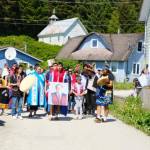 Angoon dancers and community members process down Front Street before they name and launch a dugout canoe they built with master carver Wayne Price. (Photo by Claire Stremple/Alaska Beacon)